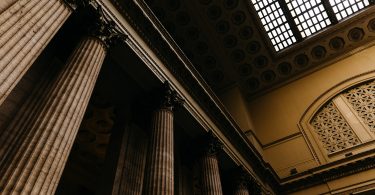 Photo of a ceiling in a courthouse with large columns and a skylight.